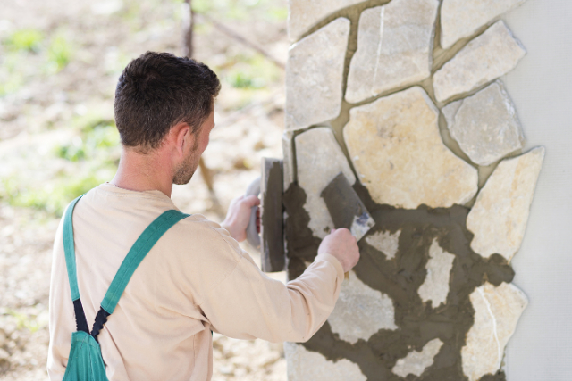 Masonry worker filling in stone wall with cement mix